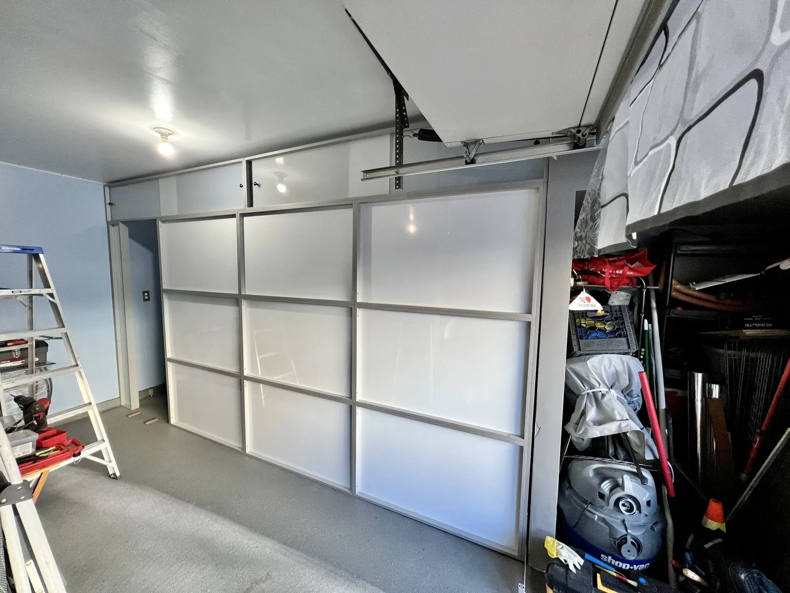 Garage room divider installed &mdash; freestanding wall with sliding door sealing a private room off from the garage-door side