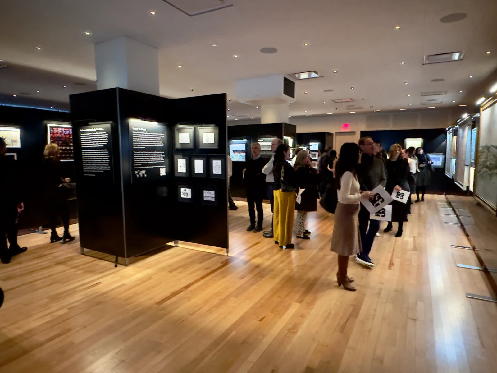 Gallery opening in a Midtown NYC event space &mdash; guests viewing framed work hung on freestanding black display walls