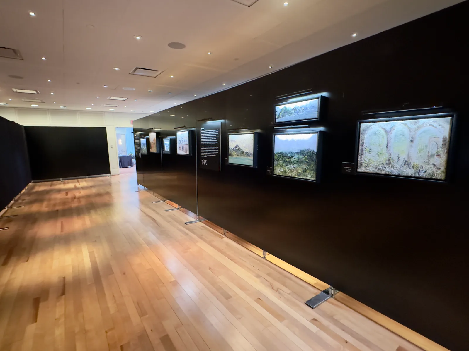 Freestanding black gallery display walls standing on floor plates in a Midtown NYC event space, art hung and lit, before guests arrive