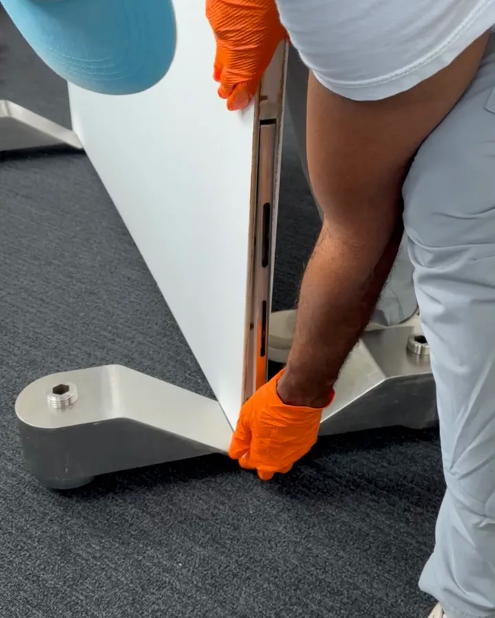 Close-up of the wall panel seated on a polished-chrome Omni-Roller leg, a gloved hand at the foot of the panel