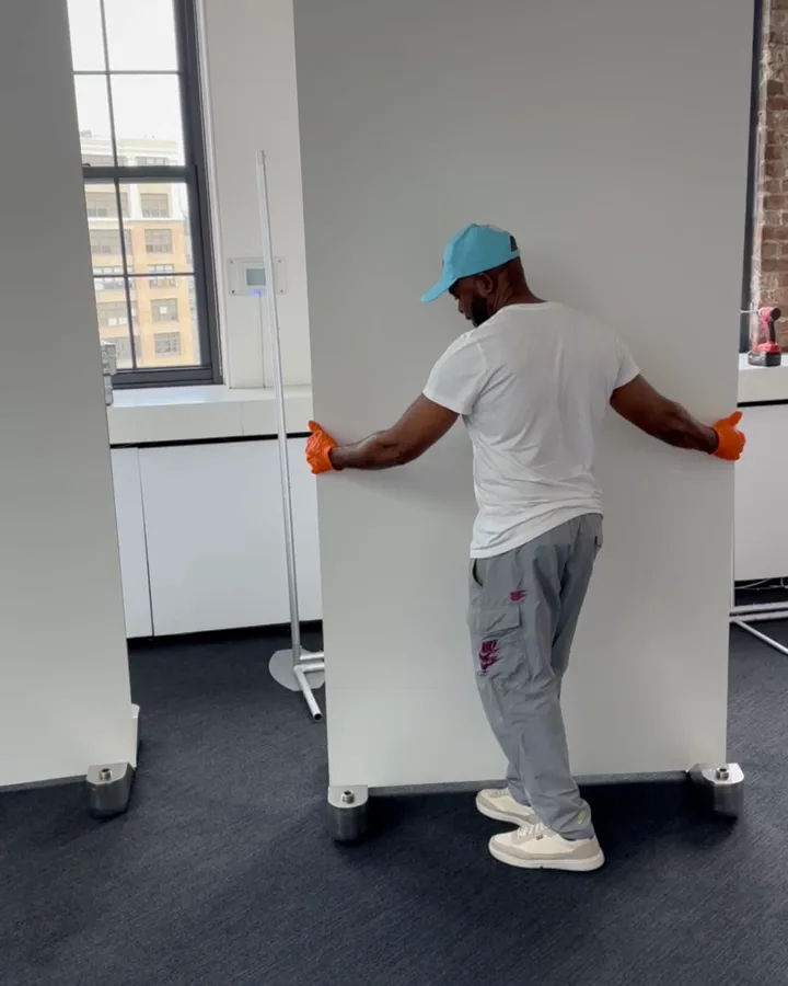 A 1W2R crew member rolling an 8 ft Omni-Roller wall across a carpeted loft office with one hand on each edge