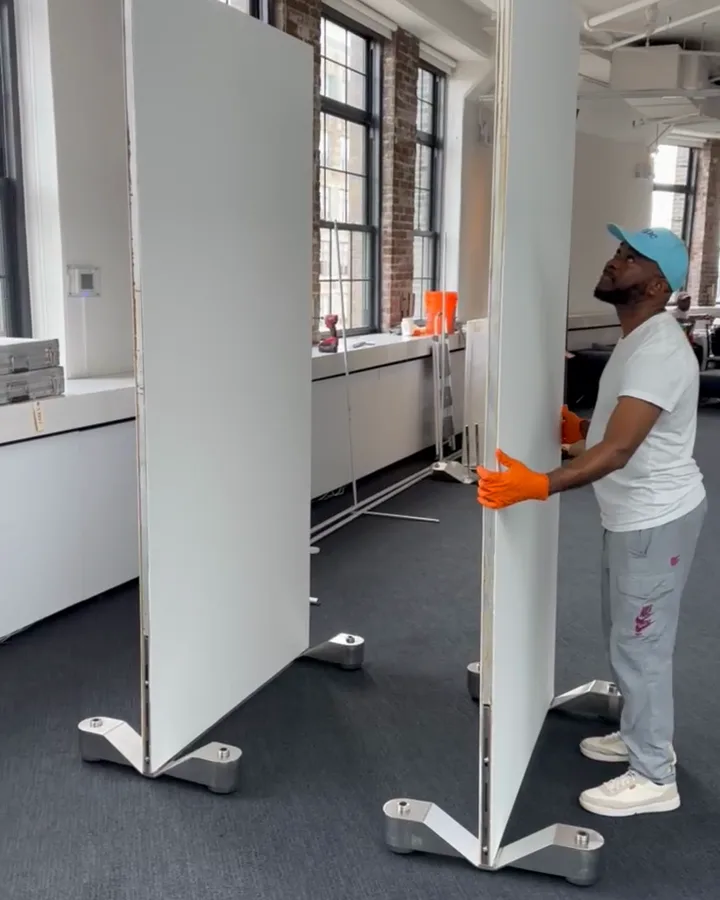 An Omni-Roller wall turned edge-on on its chrome roller legs while a crew member steadies it, a second wall behind